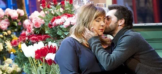 Sur scène, deux acteurs sont en présence : un homme embrasse une femme sur la joue tandis que cette dernière ferme simplement les