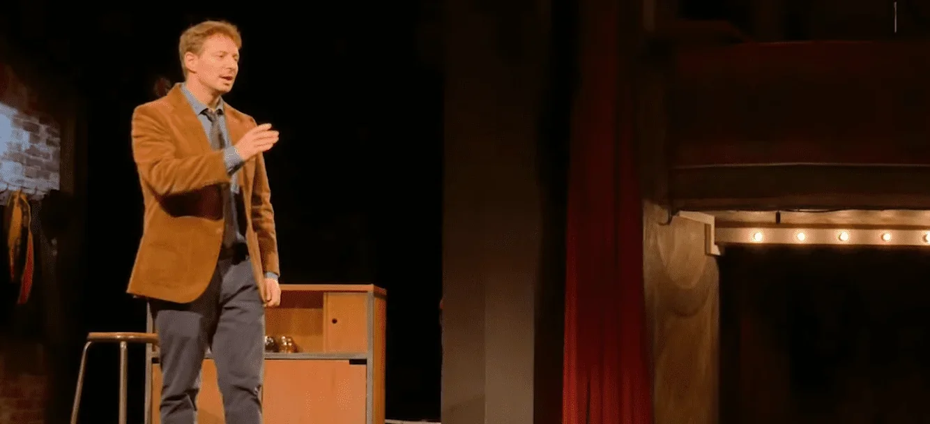 Sur scène, l'homme, protagoniste de "L'Embarras du choix" d'une pièce de théâtre , se tient debout devant le public, les yeux bril