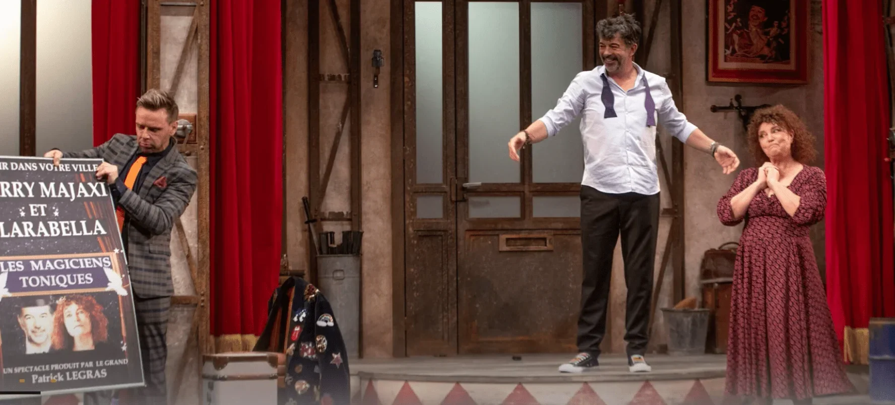 Trois acteurs se trouvent sur scène, tandis que deux d'entre eux, un homme et une femme, observent attentivement une affiche prése