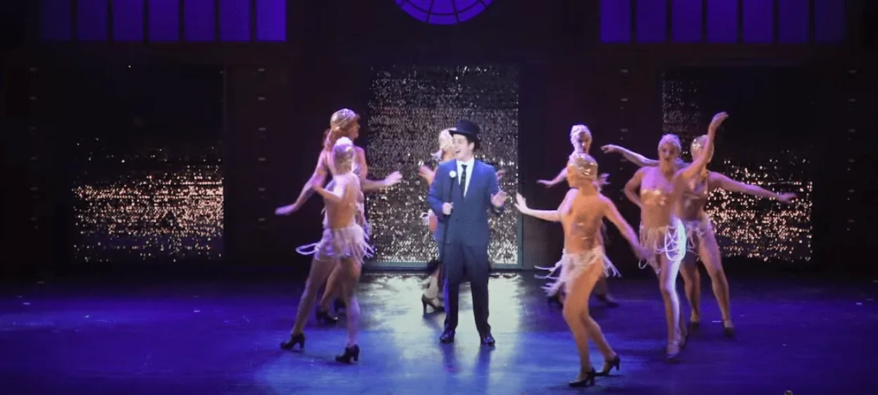 Léon est habillé de manière élégante, avec un costume noir et blanc, alors que les danseuses du ballet portent des tutus blancs. L