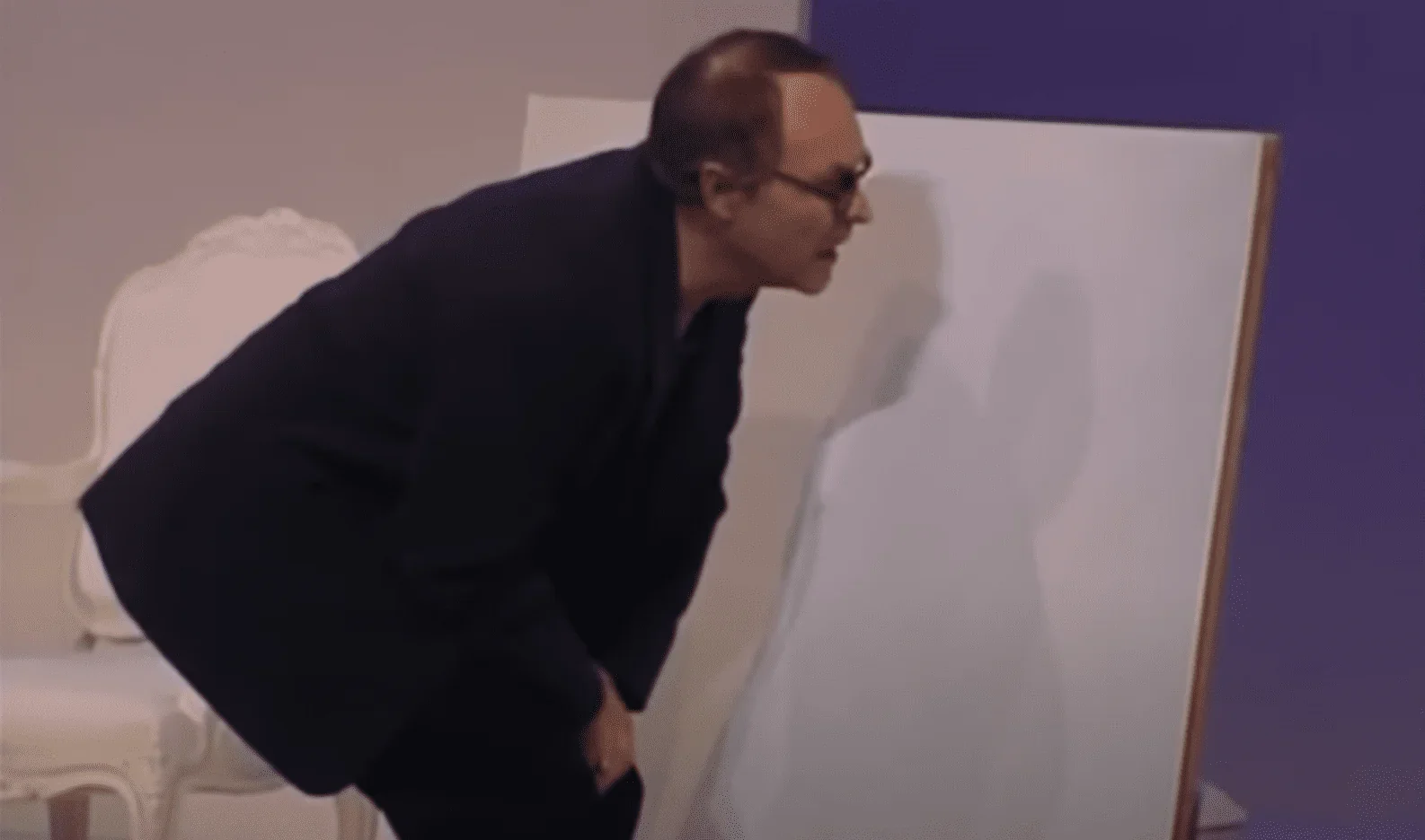 Sur la photo, nous pouvons voir un comédien sur scène en train de regarder un tableau. Le tableau est une peinture entièrement bla