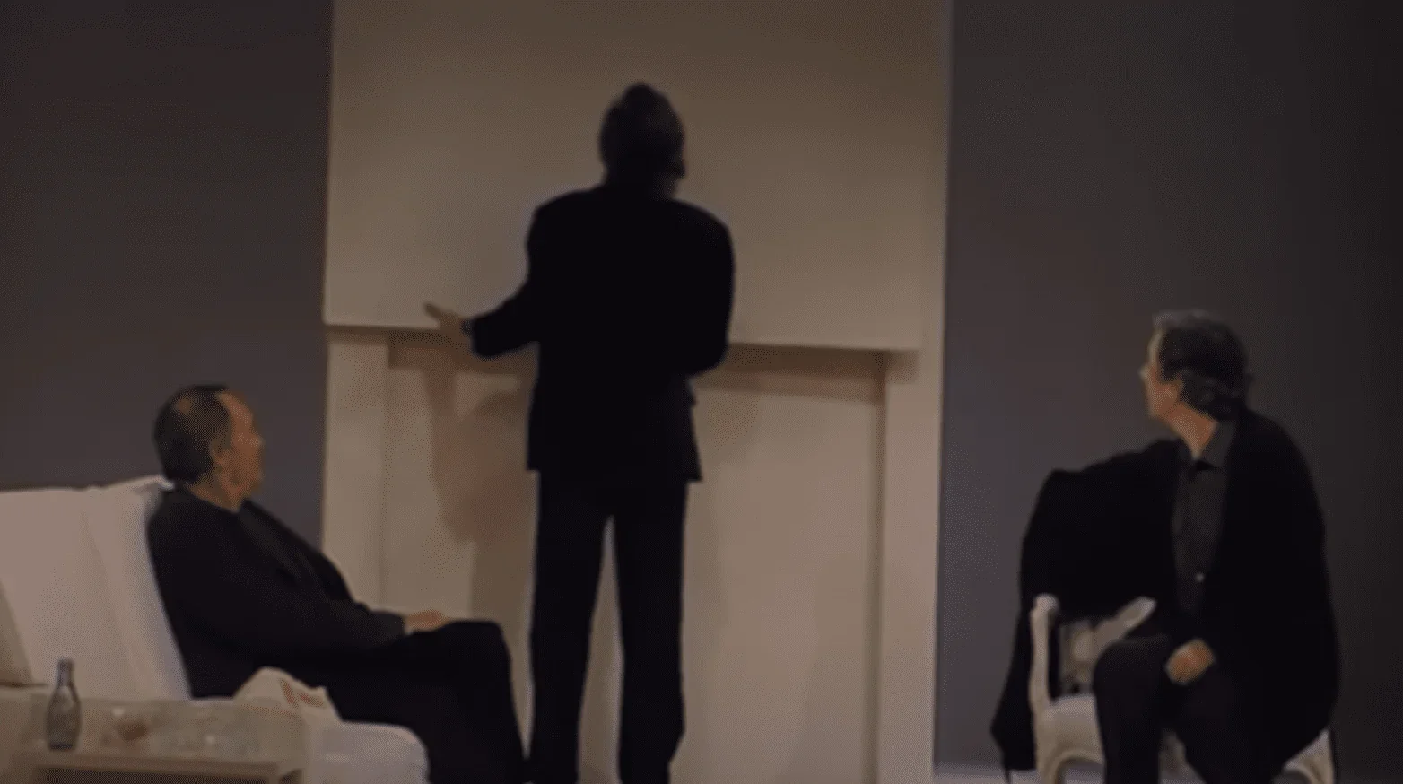 Sur cette photo, nous voyons trois amis sur scène qui font face à une situation difficile. Deux des amis sont assis sur des chaise