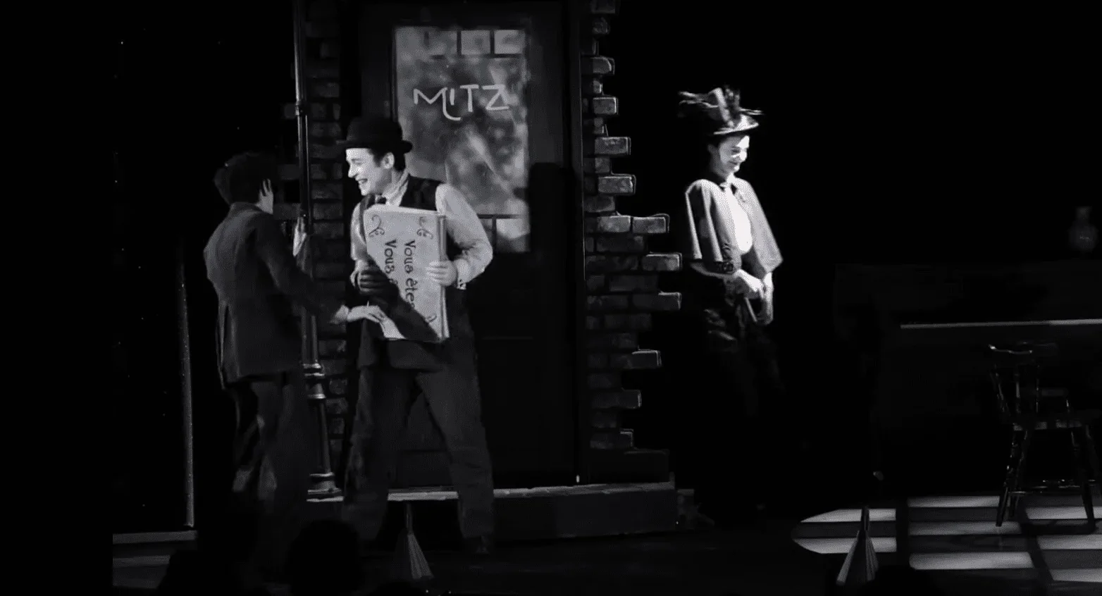 Cette photo représente le début de la pièce de théâtre "Smile", où nous voyons les trois personnages principaux se rencontrer dans