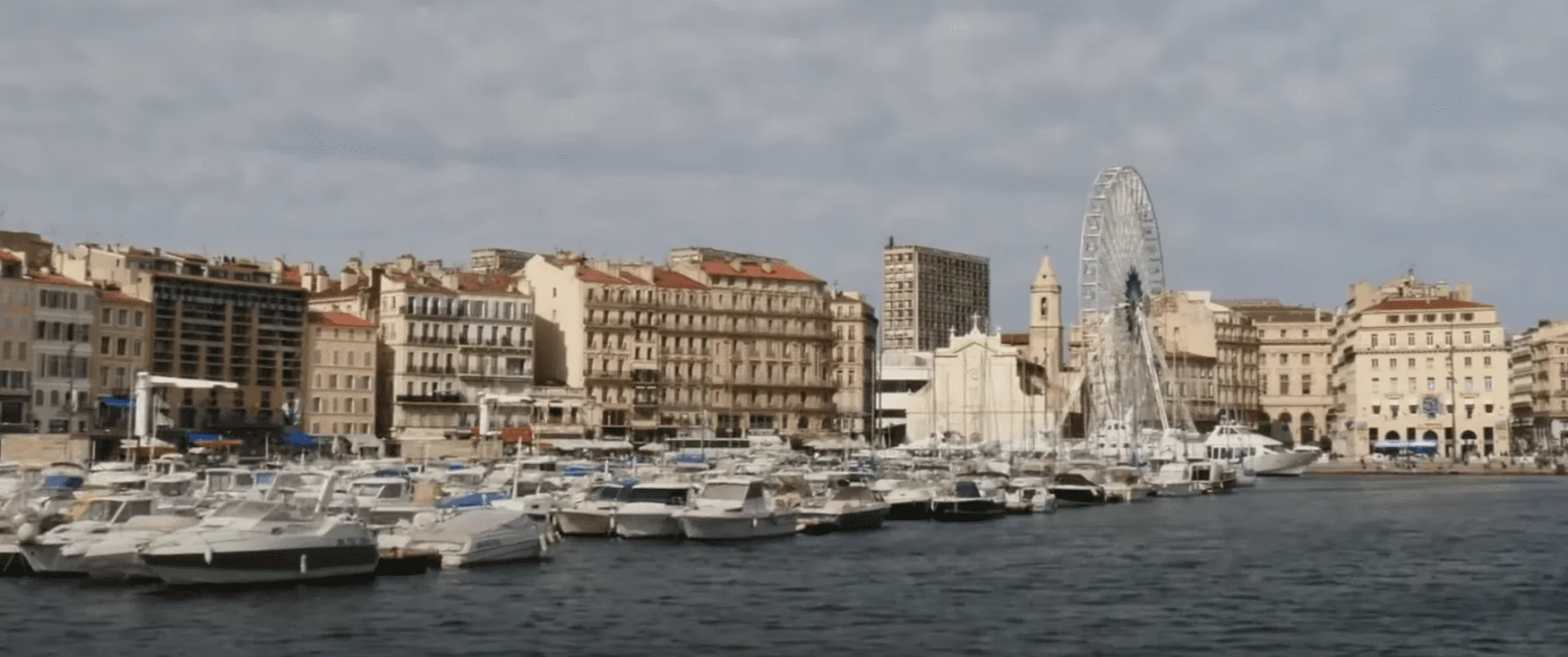 Cette image présente une vue panoramique ensoleillée de la ville côtière depuis la mer.