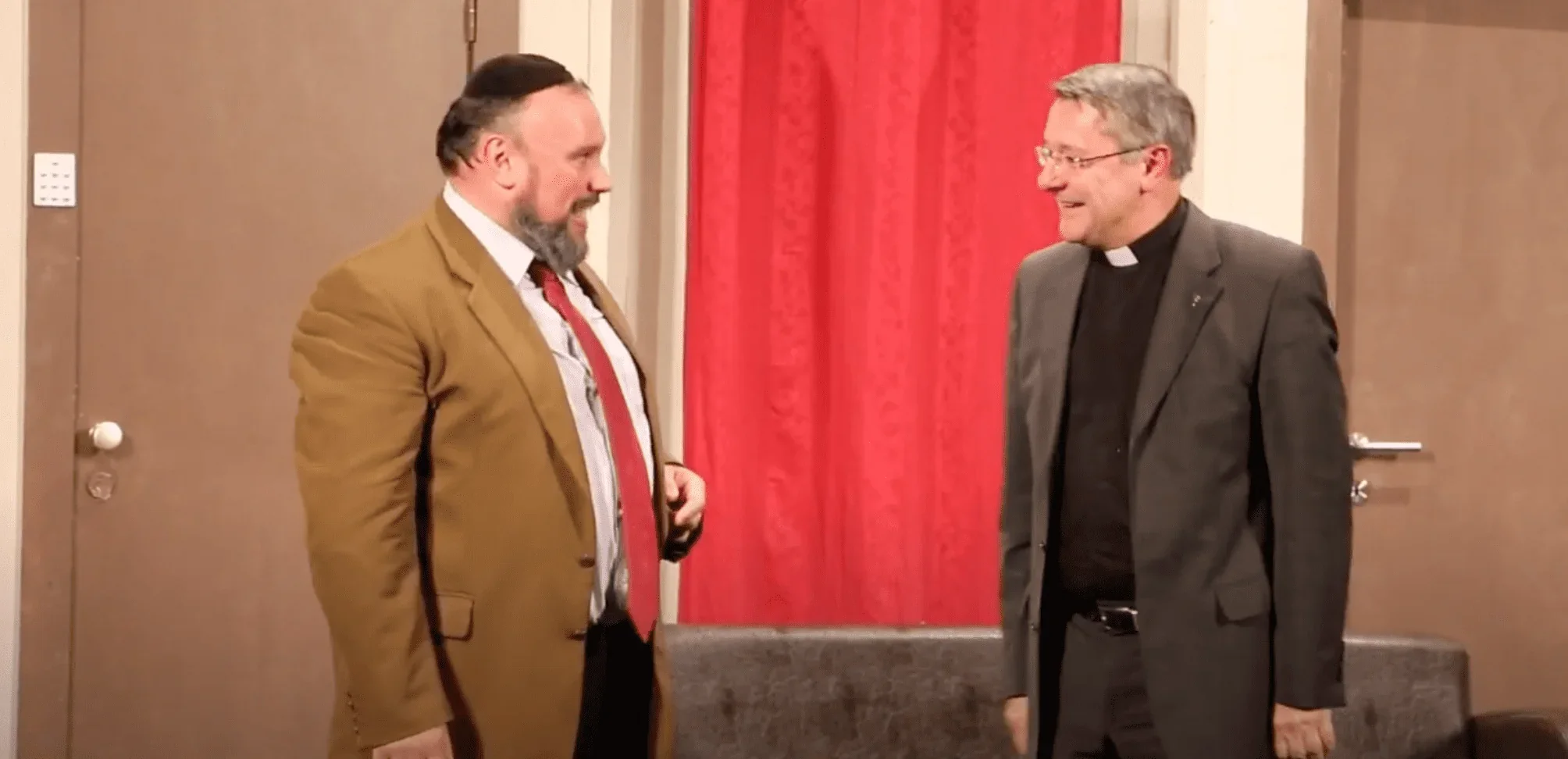 L'image met en scène un rabbin et un prêtre debout sur une scène, engagés dans une discussion animée.