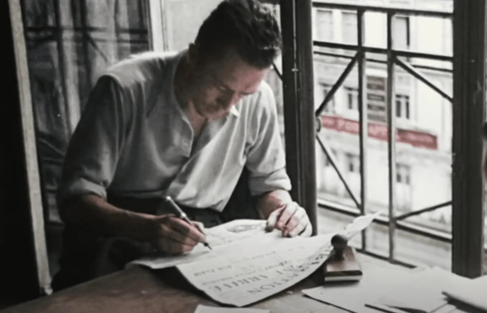 Cette image montre Albert Camus, célèbre philosophe et écrivain français, assis devant une table sur laquelle se trouvent plusieur