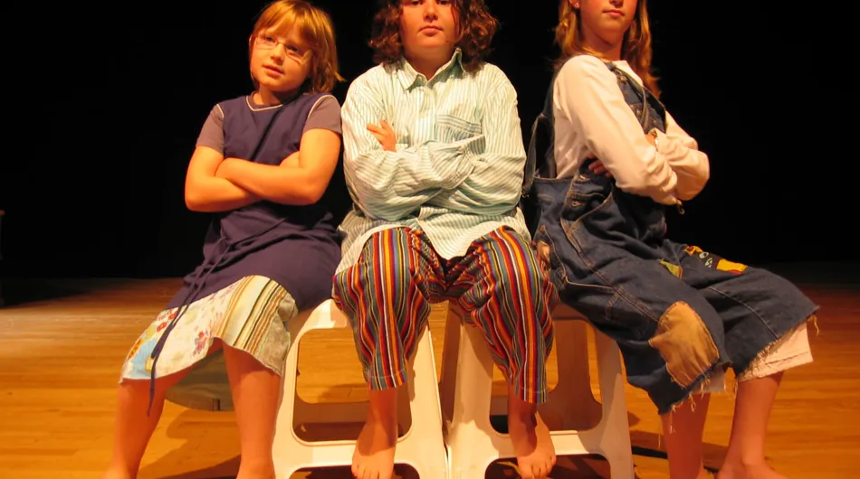 Cette photo captivante montre trois filles assises sur des tabourets, proposant une scénette remplie d'émotions. Leur talent et le